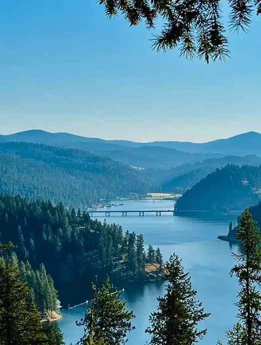 A serene lake framed by lush trees and majestic mountains under a clear blue sky