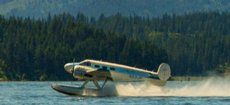A small plane takes off from the water, its wings reflecting sunlight as it ascends into the clear blue sky